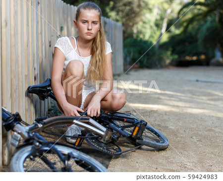 Teen girl near fence checking bicycle before ride in park Teen girl near fence checking bicycle before ride in park 59424983