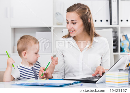 Female employee is working on laptop while child painting on papers Female employee is working on laptop while child painting on papers 59425167