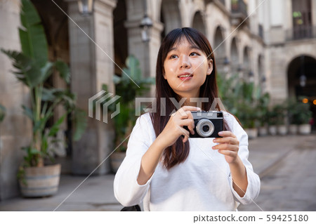 Young chinese woman traveler strolling with luggage around city, making photo of sights Young chinese woman traveler strolling with luggage around city, making photo of sights 59425180