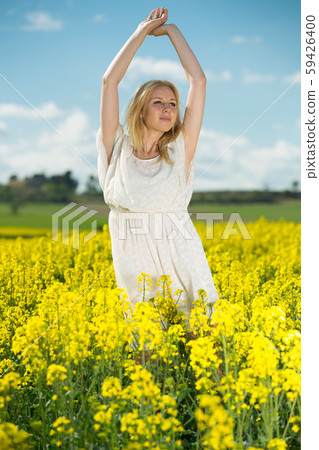Young woman in yellow oilseed rape field stretch oneself outdoor Young woman in yellow oilseed rape field stretch oneself outdoor 59426400