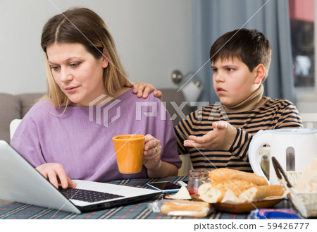 Young woman working at laptop and son trying to talking with she 59426777