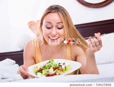 Blond woman in underwear sitting in the bed and enjoying a salad Blond woman in underwear sitting in the bed and enjoying a salad 59427608