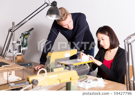 Teacher helping girl making architectural elements on scroll saw 59427796