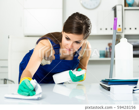 Young woman in an overalls cleans the table at office Young woman in an overalls cleans the table at office 59428156