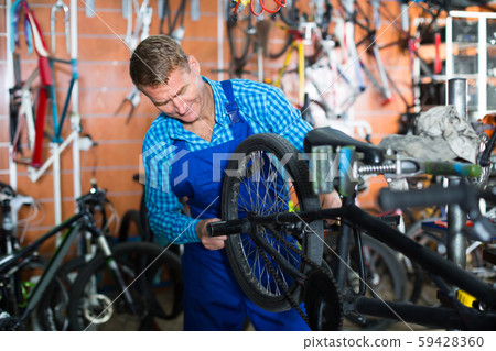 Positive man seller wearing uniform fixing bike 59428360
