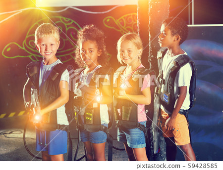 Group portrait of positive smiling teenagers with laser guns having fun on dark lasertag arena 59428585