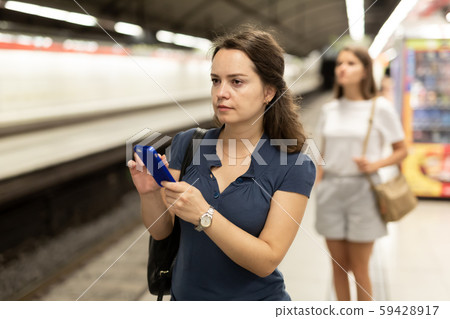 Attractive woman writes message on the phone while waiting for a subway train 59428917
