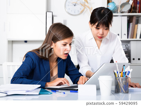 Two businesswomen sitting at desk and working together at office Two businesswomen sitting at desk and working together at office 59429095