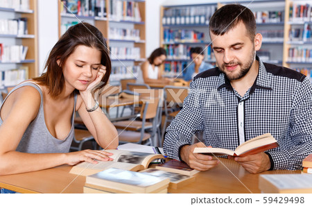 Young people reading and making notes while preparing for exam in college library Young people reading and making notes while preparing for exam in college library 59429498