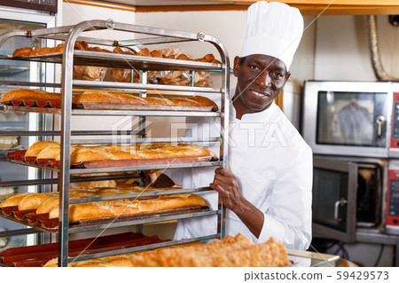 Baker carrying baked baguettes on rack Baker carrying baked baguettes on rack 59429573
