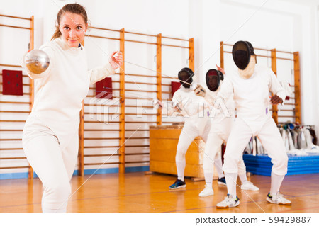 Young female fencer practicing fencing technique in training room 59429887