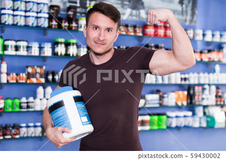 Athletic man holding sport nutrition supplements, demonstrating muscles 59430002