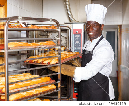 Baker putting baked baguettes on rack Baker putting baked baguettes on rack 59430119