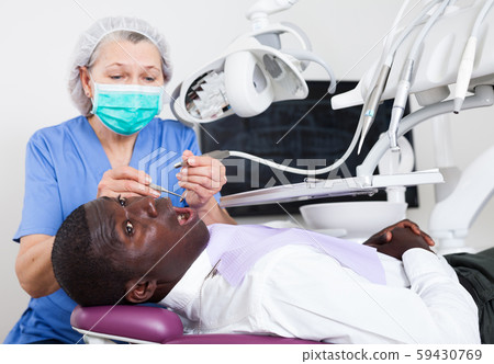 Dentist professional filling teeth for man patient sitting in medical chair Dentist professional filling teeth for man patient sitting in medical chair 59430769