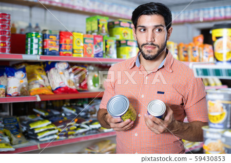 Adult male is choosing conserved peas in market. 59430853