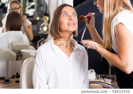 female makeup artist applying cosmetics for woman 59432450