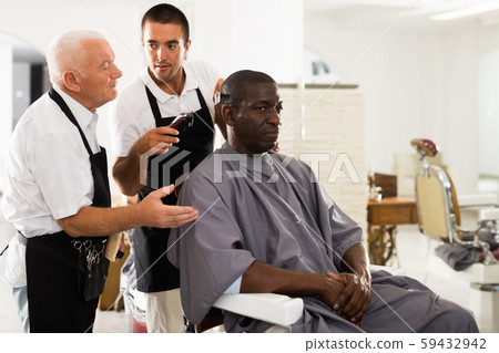 Aged barber teaching apprentice to male haircut Aged barber teaching apprentice to male haircut 59432942