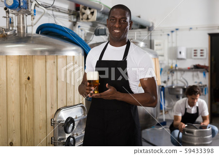 African american man brewer in apron standing with glass of beer 59433398