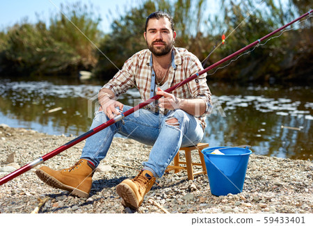 Adult male fisherman pulls fishing line on a fishing rod Adult male fisherman pulls fishing line on a fishing rod 59433401