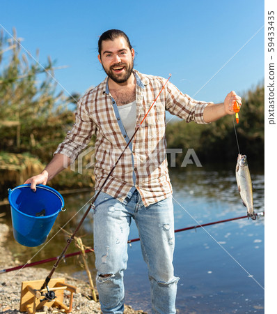 Adult man standing near river and pulling fish expressing emotions of dedication Adult man standing near river and pulling fish expressing emotions of dedication 59433435
