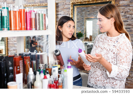 Young women attentively looking hair care products at beauty salon Young women attentively looking hair care products at beauty salon 59433593