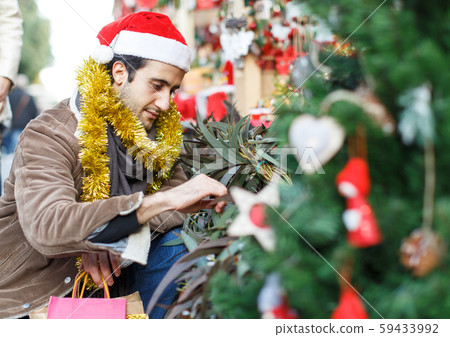 Young man in Christmas hat buying decoration at Christmas Fair outside Young man in Christmas hat buying decoration at Christmas Fair outside 59433992