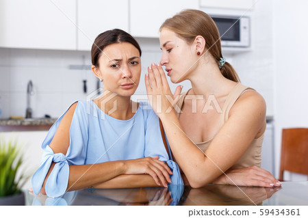 Portrait of sad young girlfriends whispers in the ear and sharing secrets Portrait of sad young girlfriends whispers in the ear and sharing secrets 59434361