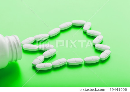 Calcium vitamin in the form of a tooth spilled out of a white jar on a Green background. Calcium vitamin in the form of a tooth spilled out of a white jar on a Green background. 59441906