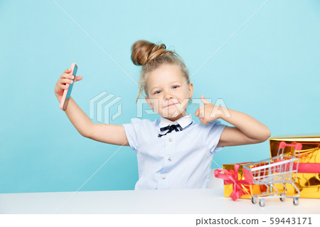 Little cute blogger making selfie on the phone sititng with a lot of presents on the table. Little cute blogger making selfie on the phone sititng with a lot of presents on the table. 59443171