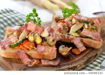 Toast with fried white asparagus, other vegetables and bacon, served on a wooden board 59446320