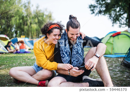 Young couple with smartphone at summer festival, sitting on the ground. 59446370