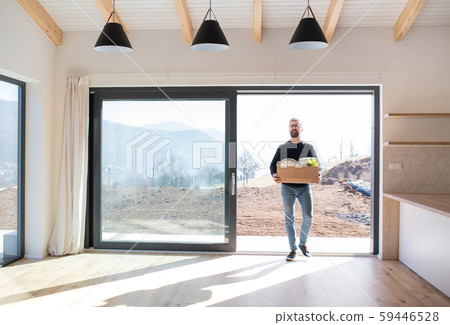 Mature man walking in unfurnished house, holding a moving box. Mature man walking in unfurnished house, holding a moving box. 59446528