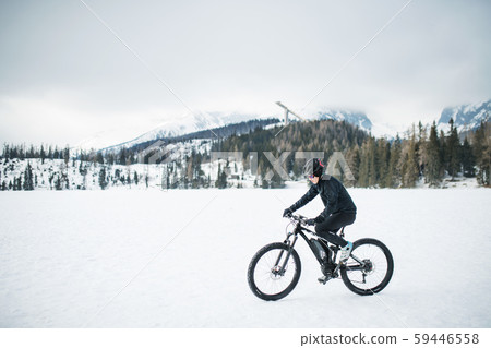 Side view of mountain biker riding in snow outdoors in winter nature. Side view of mountain biker riding in snow outdoors in winter nature. 59446558