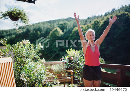 A senior woman standing outdoors on a terrace in summer, doing exercise. 59446670