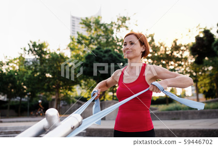Young woman doing exercise outdoors in city with elastic bands. 59446702