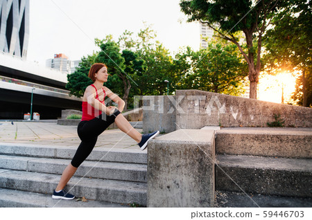 Young woman doing exercise outdoors in city at sunset, stretching. 59446703
