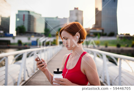 Young woman with smartphone resting after doing exercise on bridge outdoors in city. 59446705