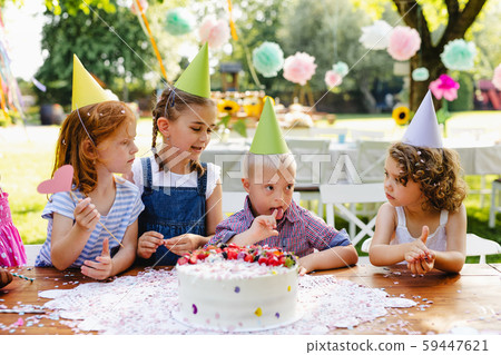 Down syndrome child with friends on birthday party outdoors in garden. Down syndrome child with friends on birthday party outdoors in garden. 59447621