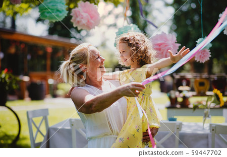 Grandmother holding small girll outdoors on garden party in summer. Grandmother holding small girll outdoors on garden party in summer. 59447702