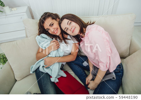 Two shopaholic girls sitting on the sofa, smiling, looking at the camera, enjoying clothes they have 59448190