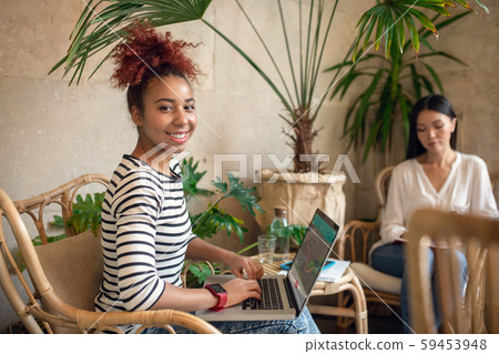 Curly businesswoman using laptop while sitting near friend Curly businesswoman using laptop while sitting near friend 59453948