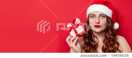 Beautiful woman in santa hat holding present box with satin ribbon bow look at camera on red Beautiful woman in santa hat holding present box with satin ribbon bow look at camera on red 59456036
