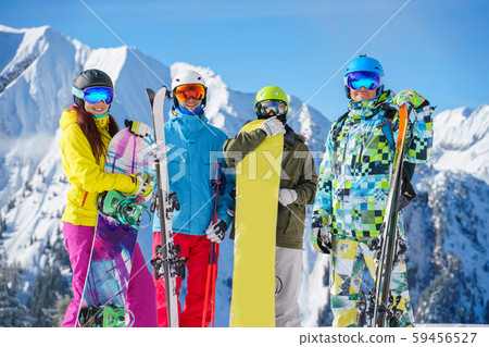 Image of two sports women and two men with skis and snowboard standing at ski resort 59456527