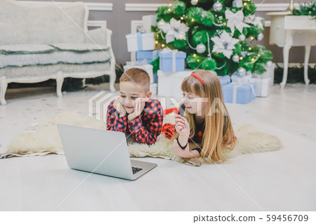 Joyful kids are playing modern interesting games on laptop in room decorated for new year. 59456709