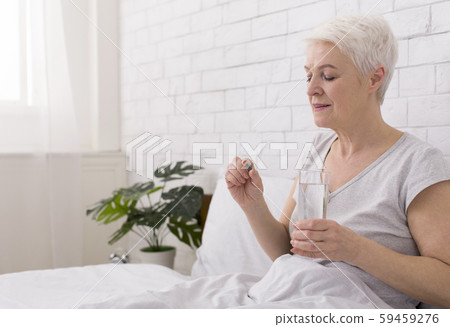Healthy senior woman holding pills and glass of water Healthy senior woman holding pills and glass of water 59459276