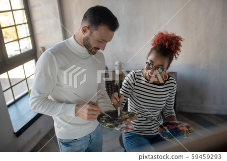 Smiling girlfriend taking paints while painting with beloved 59459293