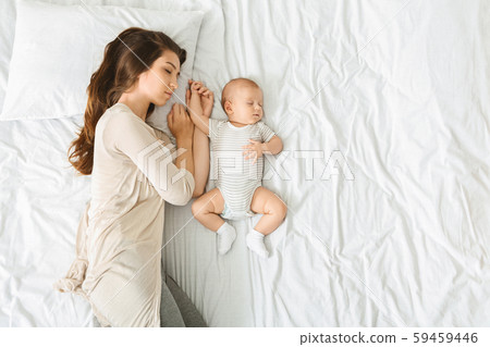 Tired mother sleeping in bed with baby by her side Tired mother sleeping in bed with baby by her side 59459446