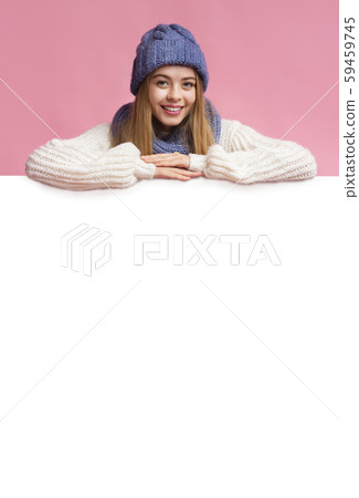 Blonde girl in winter hat leaning on blank board Blonde girl in winter hat leaning on blank board 59459745