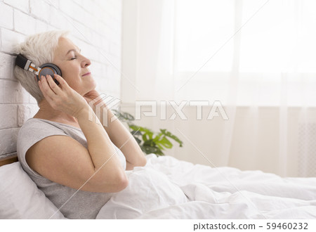 Tranquil senior lady listening to audiobook in bed Tranquil senior lady listening to audiobook in bed 59460232