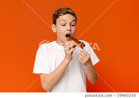 Teenage guy enjoying chocolate eclair, orange background Teenage guy enjoying chocolate eclair, orange background 59460258